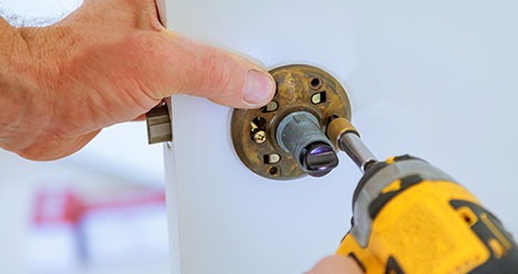 handyman installing a doornob with power tools